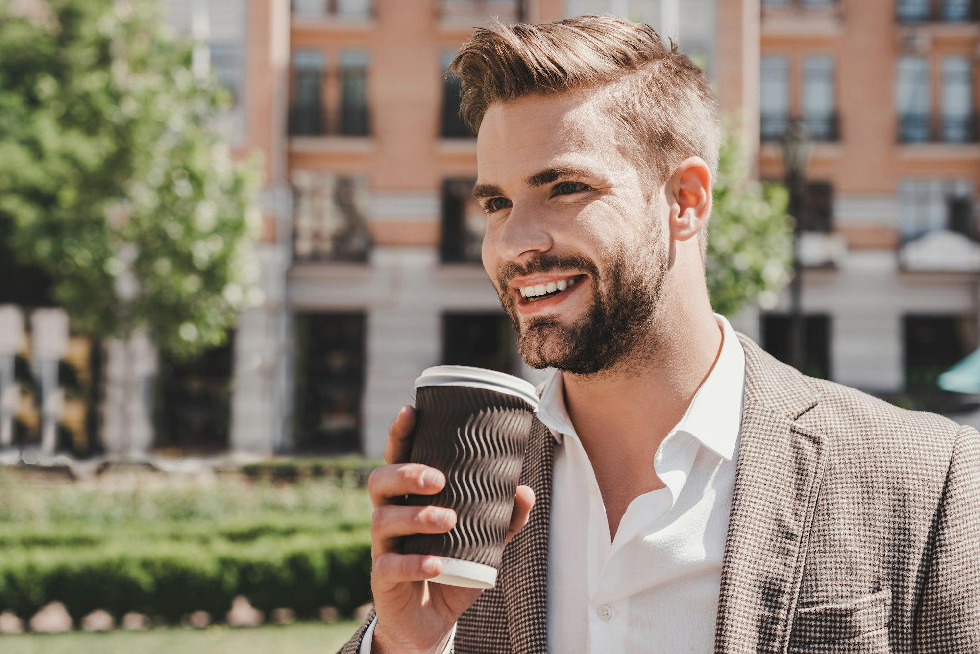 Coffee time. Portrait of confident brown-haired man holding coffee cup and smiling aside while